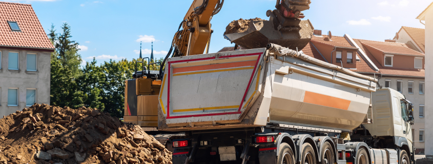 İnşaat sahasında atık ve molozları damperli kamyona yükleyen ağır ekskavatör makinesi. Bina söküm ve inşaat atıkları bertaraf hizmeti. Şantiye endüstriyel arka plan - Sorglos Bauen GmbH