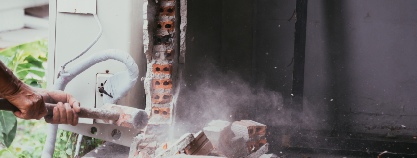 Unrecognizable builder using a sledgehammer breaking and smashing the wall fallen into debris - breaking wall and challenges concept - Sorglos Bauen GmbH